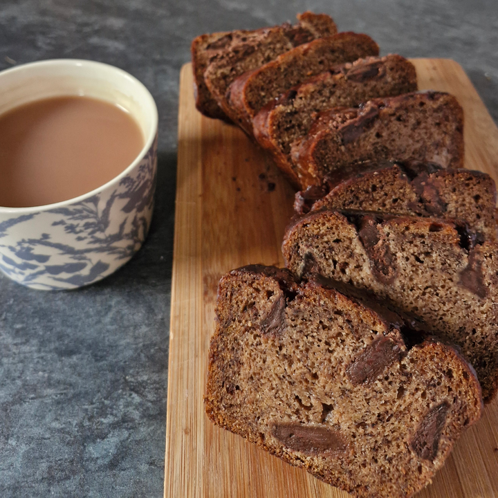 Slices of chocolate chip bread arranged on a wooden cutting board next to a blue and white patterned cup of coffee on a gray stone surface.