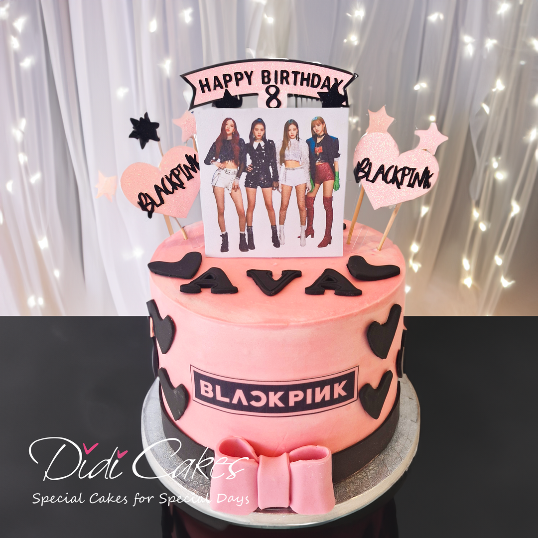 A two-tier birthday cake decorated in pink with BlackPink band members' images, hearts, and text decorations.