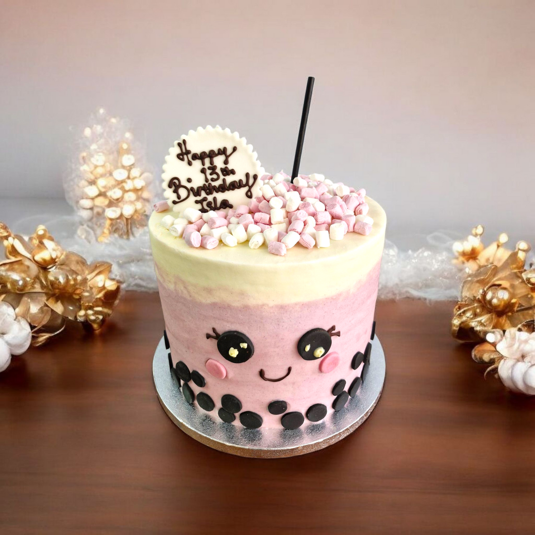 Bubble Tea Birthday cake with pink and white frosting, black polka dots, and a straw on a wooden table.